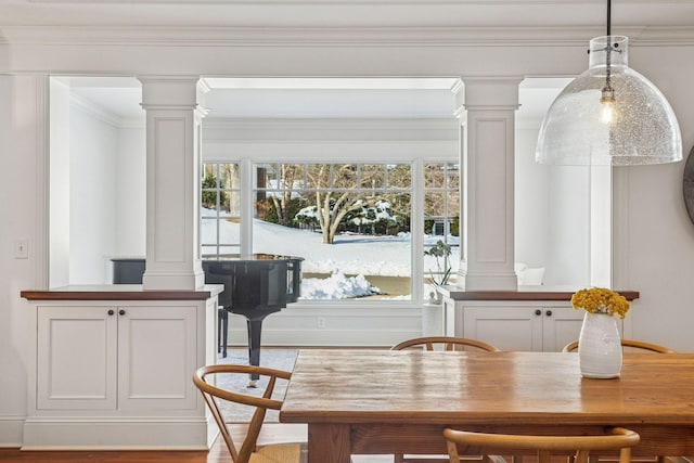 dining area with decorative columns, wood finished floors, and ornamental molding