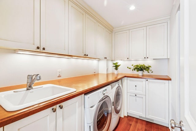 washroom with visible vents, washer and dryer, a sink, wood finished floors, and cabinet space