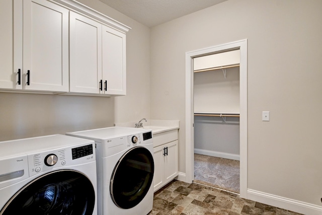 washroom with cabinet space, baseboards, stone finish floor, washing machine and clothes dryer, and a sink