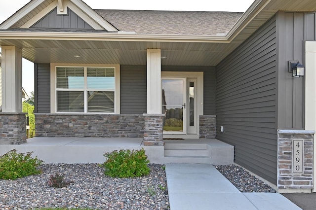 doorway to property with board and batten siding, covered porch, roof with shingles, and stone siding