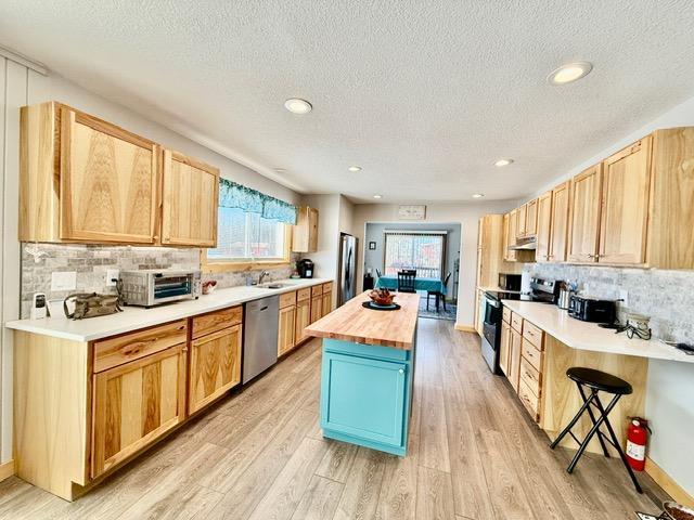 kitchen featuring light wood finished floors, butcher block counters, a center island, stainless steel appliances, and under cabinet range hood