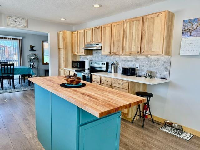 kitchen featuring stainless steel electric range oven, butcher block counters, light brown cabinetry, black microwave, and under cabinet range hood