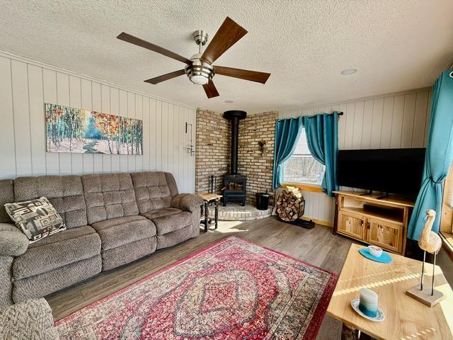 living area with a ceiling fan, a wood stove, a textured ceiling, and wood finished floors