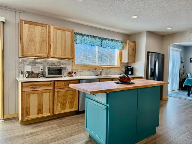 kitchen featuring a toaster, stainless steel appliances, wooden counters, backsplash, and light wood-style flooring