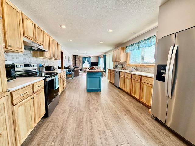 kitchen with light wood-style flooring, appliances with stainless steel finishes, open floor plan, under cabinet range hood, and backsplash