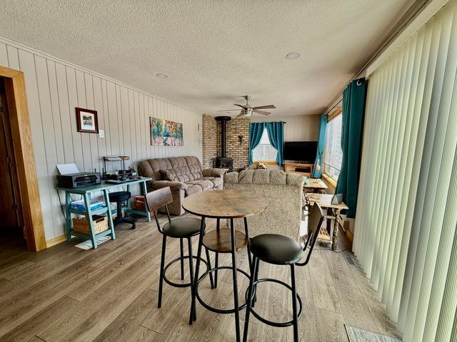 dining area with a textured ceiling, a ceiling fan, a wood stove, and light wood-style floors