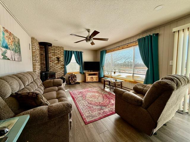 living room with a wood stove, ceiling fan, a textured ceiling, and wood finished floors