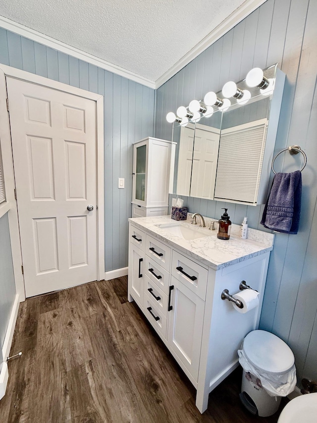 bathroom featuring a textured ceiling, wood finished floors, vanity, baseboards, and ornamental molding