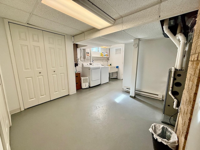 below grade area featuring a drop ceiling, a baseboard radiator, a sink, visible vents, and washer and clothes dryer