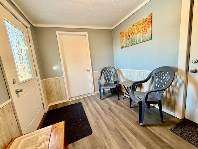 sitting room featuring crown molding, a textured ceiling, wood finished floors, and wainscoting