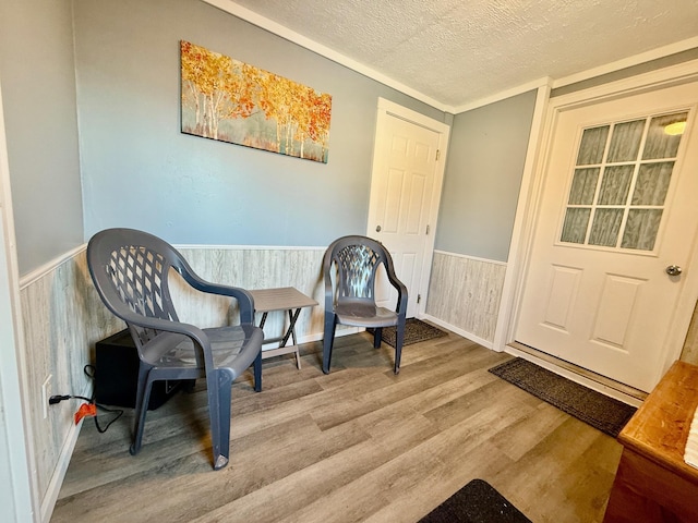 sitting room with a wainscoted wall, a textured ceiling, wood finished floors, and wooden walls