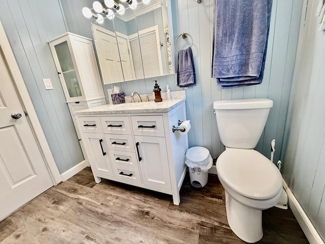 bathroom featuring wooden walls, wood finished floors, toilet, and vanity