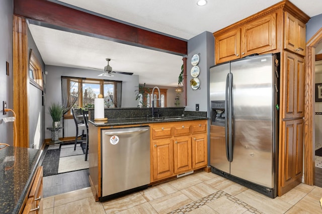 kitchen with dark stone countertops, brown cabinets, appliances with stainless steel finishes, a peninsula, and a sink