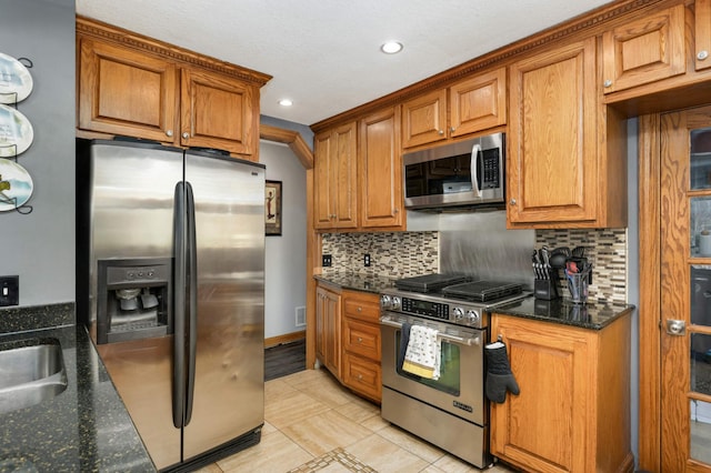 kitchen with tasteful backsplash, brown cabinets, appliances with stainless steel finishes, and dark stone countertops