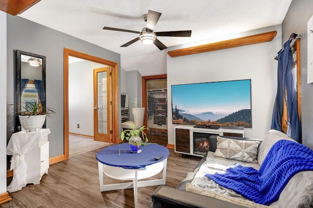 living room with a glass covered fireplace, baseboards, a textured ceiling, and wood finished floors