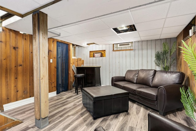 living area with a dry bar, wooden walls, wood finished floors, and a drop ceiling