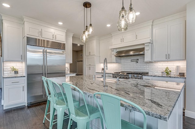 kitchen featuring dark wood finished floors, stainless steel built in refrigerator, white cabinets, and a sink