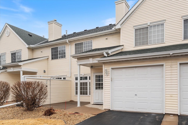 exterior space featuring a garage, a shingled roof, a chimney, and aphalt driveway