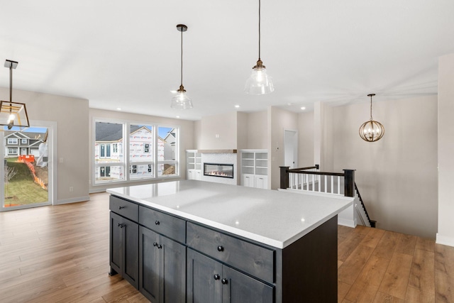 kitchen with pendant lighting, light wood finished floors, light countertops, an inviting chandelier, and a glass covered fireplace