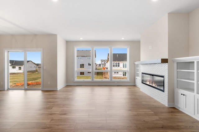 unfurnished living room featuring baseboards, a tiled fireplace, wood finished floors, and recessed lighting