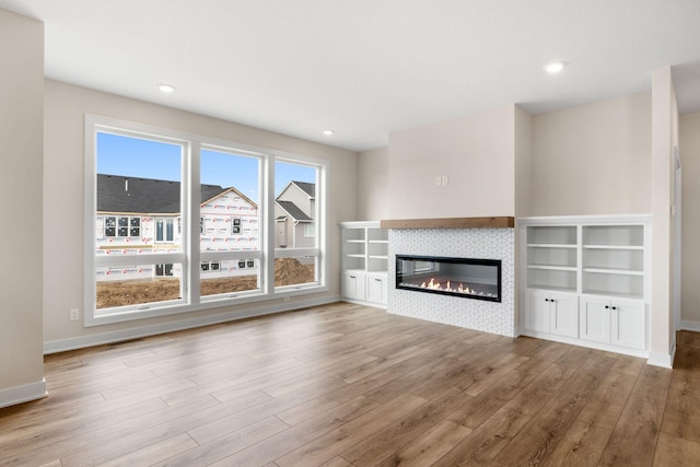 unfurnished living room with a tile fireplace, recessed lighting, baseboards, and wood finished floors