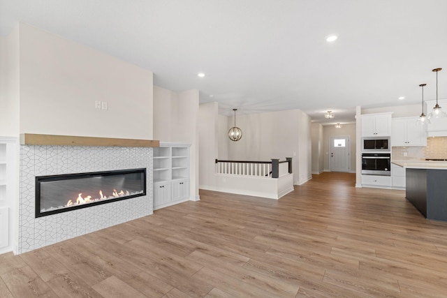 unfurnished living room featuring light wood-style floors, recessed lighting, a notable chandelier, and a fireplace