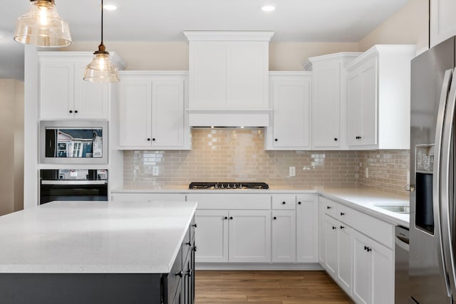 kitchen featuring stainless steel appliances, hanging light fixtures, decorative backsplash, light wood-style floors, and white cabinets