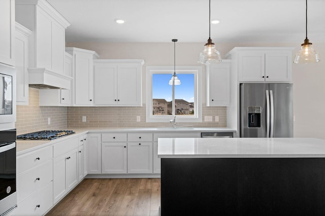 kitchen with stainless steel appliances, light countertops, light wood-type flooring, white cabinetry, and a sink