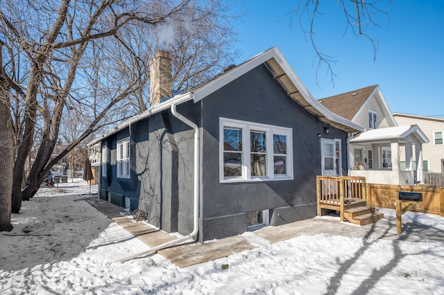 snow covered property with a chimney and stucco siding