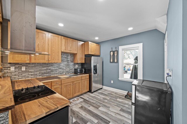 kitchen with stainless steel appliances, decorative backsplash, light wood-style floors, a sink, and extractor fan