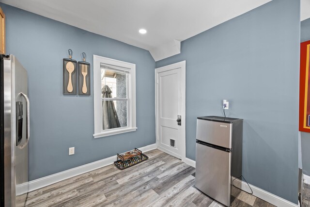 interior space featuring stainless steel refrigerator with ice dispenser, wood finished floors, freestanding refrigerator, and baseboards