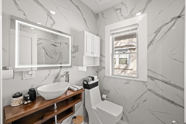 bathroom with toilet, stone wall, and vanity