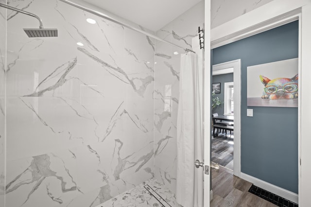 bathroom featuring a marble finish shower, baseboards, and wood finished floors