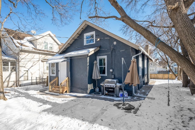 snow covered house featuring entry steps, fence, and stucco siding