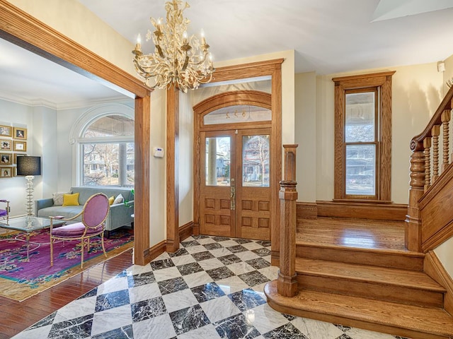 entrance foyer with baseboards, stairs, ornamental molding, wood finished floors, and a notable chandelier