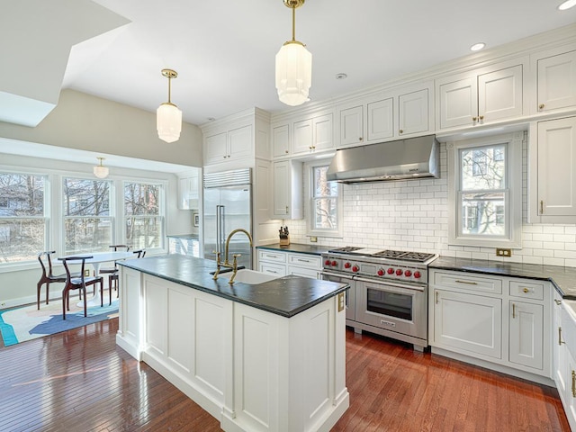 kitchen with dark wood-type flooring, under cabinet range hood, a sink, dark countertops, and high end appliances