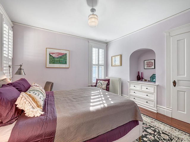 bedroom with radiator heating unit, wood finished floors, and ornamental molding