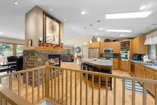 kitchen with light wood-style flooring, appliances with stainless steel finishes, vaulted ceiling, a fireplace, and a sink