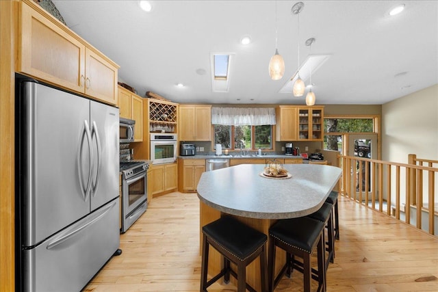 kitchen with light brown cabinets, a sink, light wood-style floors, appliances with stainless steel finishes, and a kitchen bar