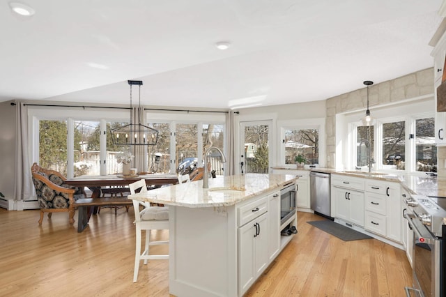 kitchen with appliances with stainless steel finishes, a sink, light stone counters, and light wood finished floors