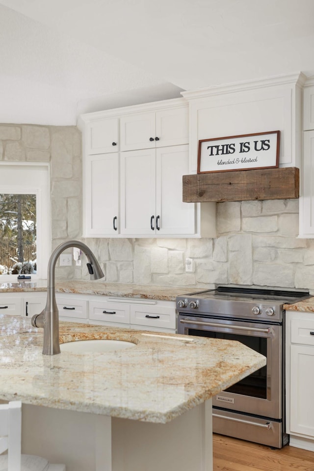 kitchen featuring white cabinets, stainless steel electric range oven, backsplash, and a sink