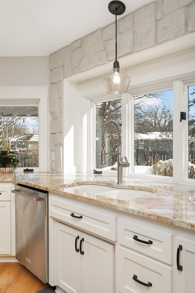 kitchen featuring light stone counters, stainless steel dishwasher, light wood-style floors, white cabinetry, and a sink