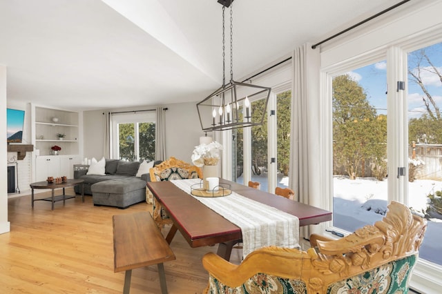 dining space featuring built in shelves, a brick fireplace, light wood-style flooring, and an inviting chandelier