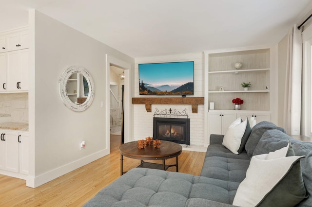 living area featuring built in shelves, a brick fireplace, baseboards, and light wood finished floors