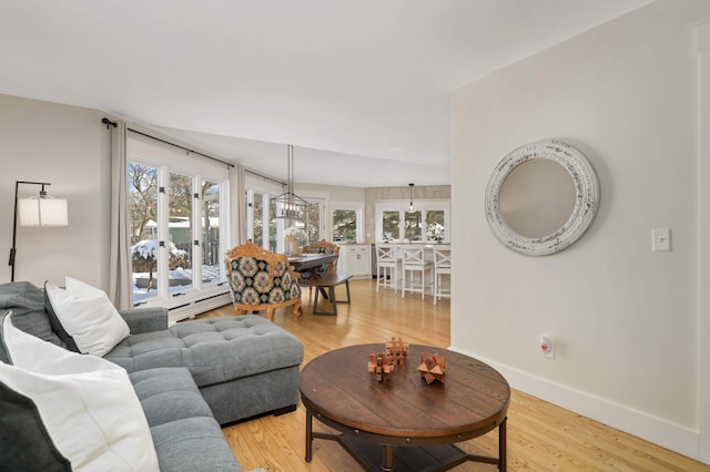 living room with a notable chandelier, light wood-type flooring, a baseboard radiator, and baseboards