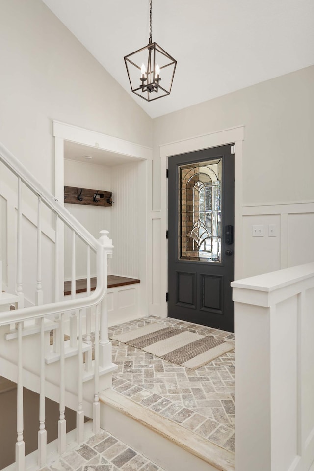 foyer entrance with brick floor, a decorative wall, stairs, vaulted ceiling, and wainscoting