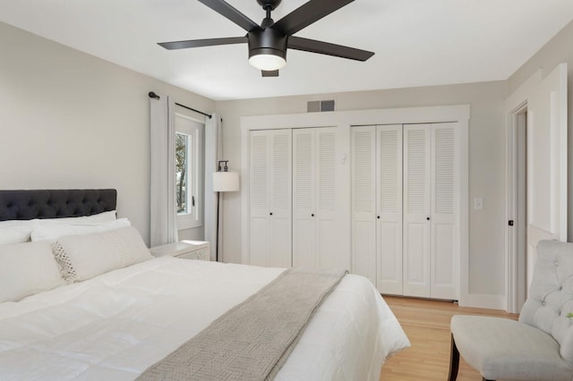 bedroom with light wood finished floors, two closets, visible vents, a ceiling fan, and baseboards