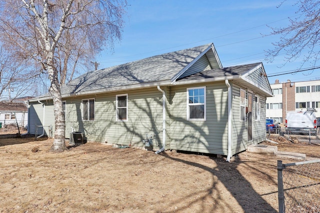 rear view of house featuring central air condition unit, fence, and roof with shingles