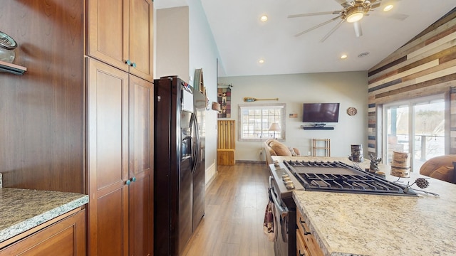 kitchen with open floor plan, light wood-style flooring, stainless steel range with gas cooktop, and black refrigerator with ice dispenser