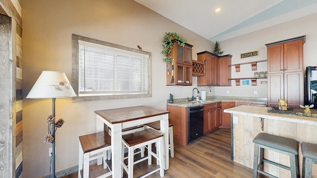 kitchen featuring dishwasher, vaulted ceiling, brown cabinets, wood finished floors, and a sink